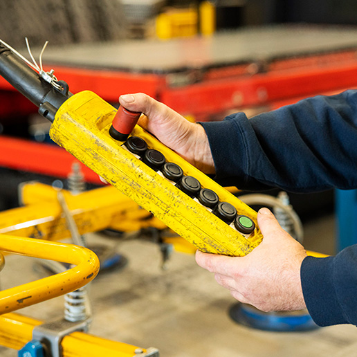 A crane operator's hands and chest holding a pendant controller that operates a crane